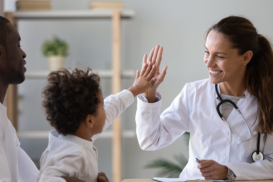 Life and Health Insurance - Family at the Doctor's Office with a Young Child High Fiving Physician and Smiling while in Father's Lap